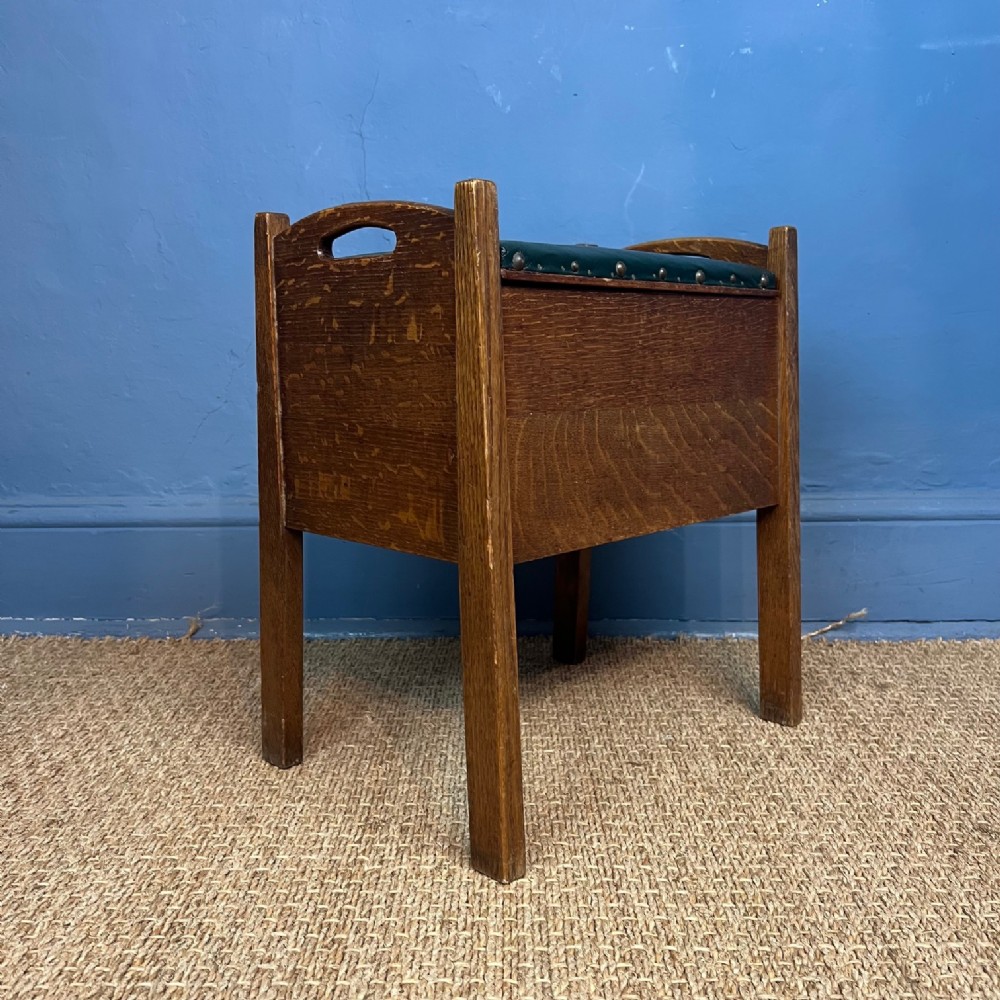 A 1930s Gordon Russell oak stool featuring a green leather padded top with brass studding and integrated side handles.