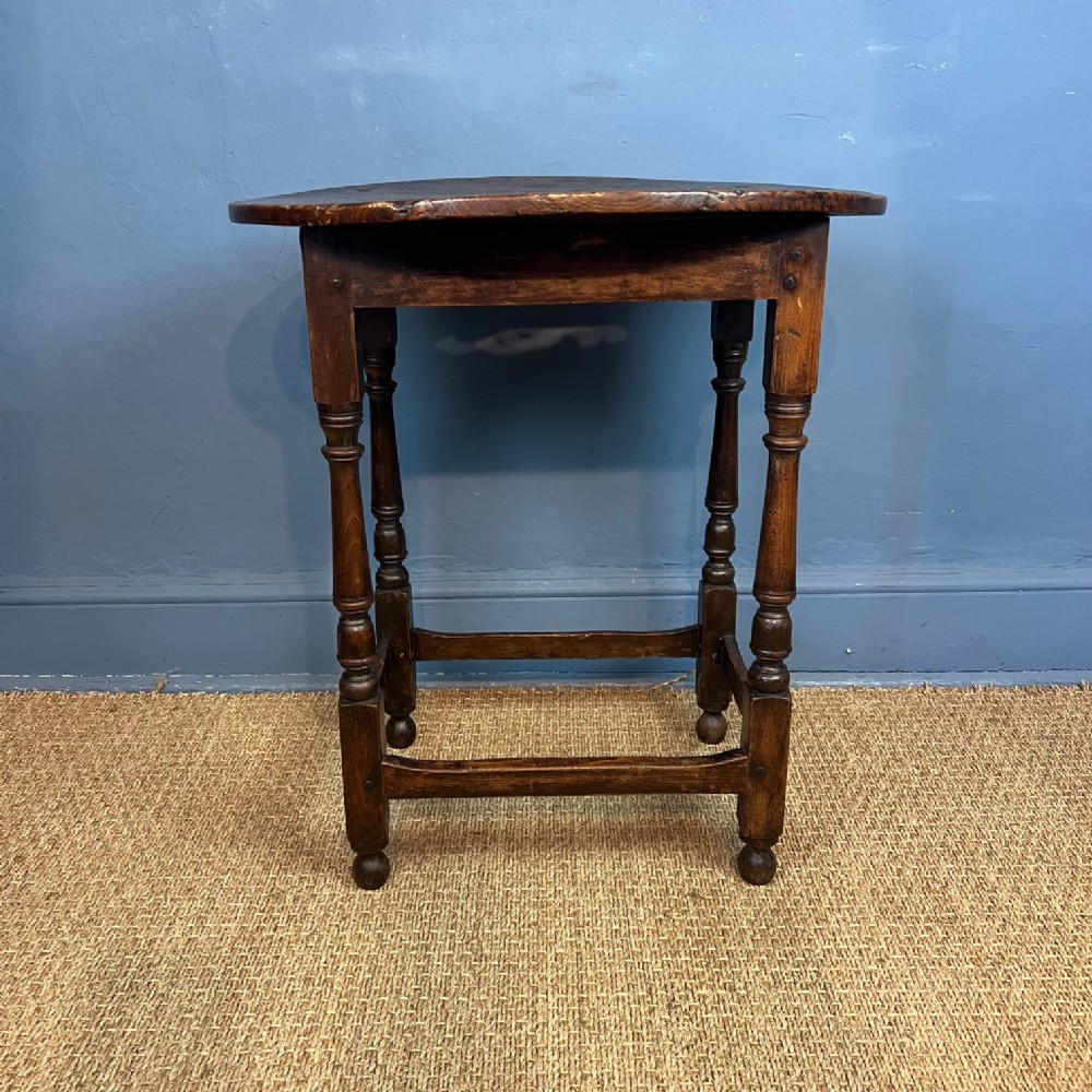 An early eighteenth-century dark oak side table featuring an oval top, turned legs, and perimeter box stretchers.
