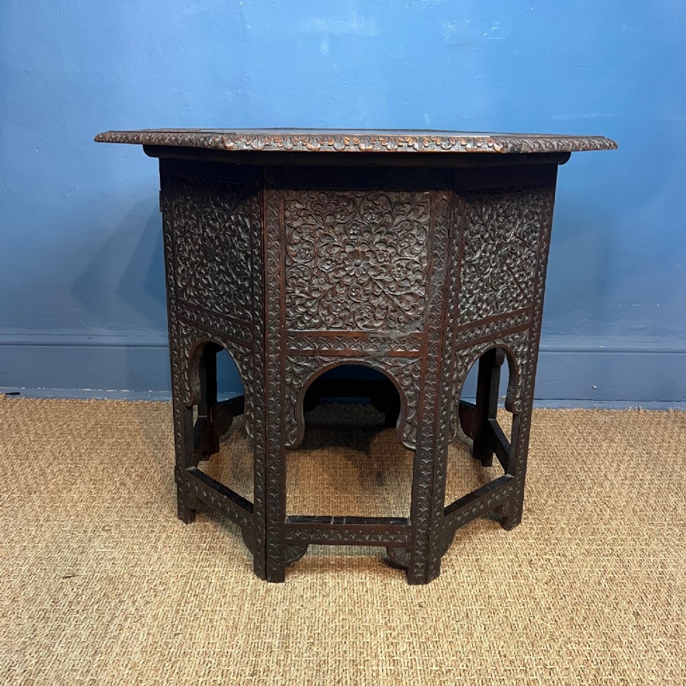 A late 19th-century dark hardwood octagonal side table featuring dense floral hand-carvings and arched panel legs.