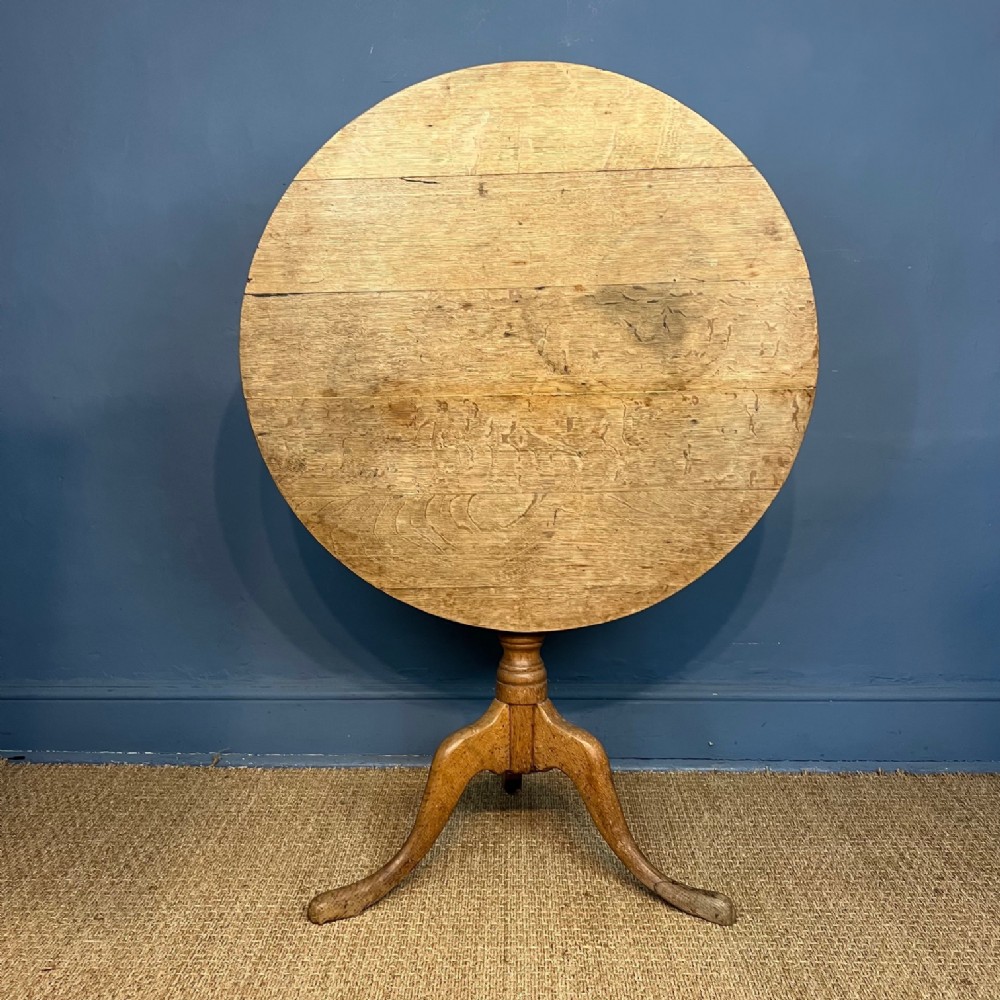 A late Georgian circular tilt-top table made from pale oak with a turned central column and three splayed legs.