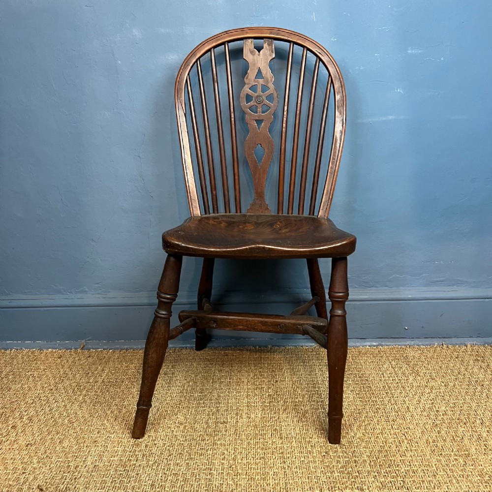 A mid-19th-century yew and elm Windsor chair featuring a wheelback splat, arched hoop back, contoured saddle seat, and turned legs.