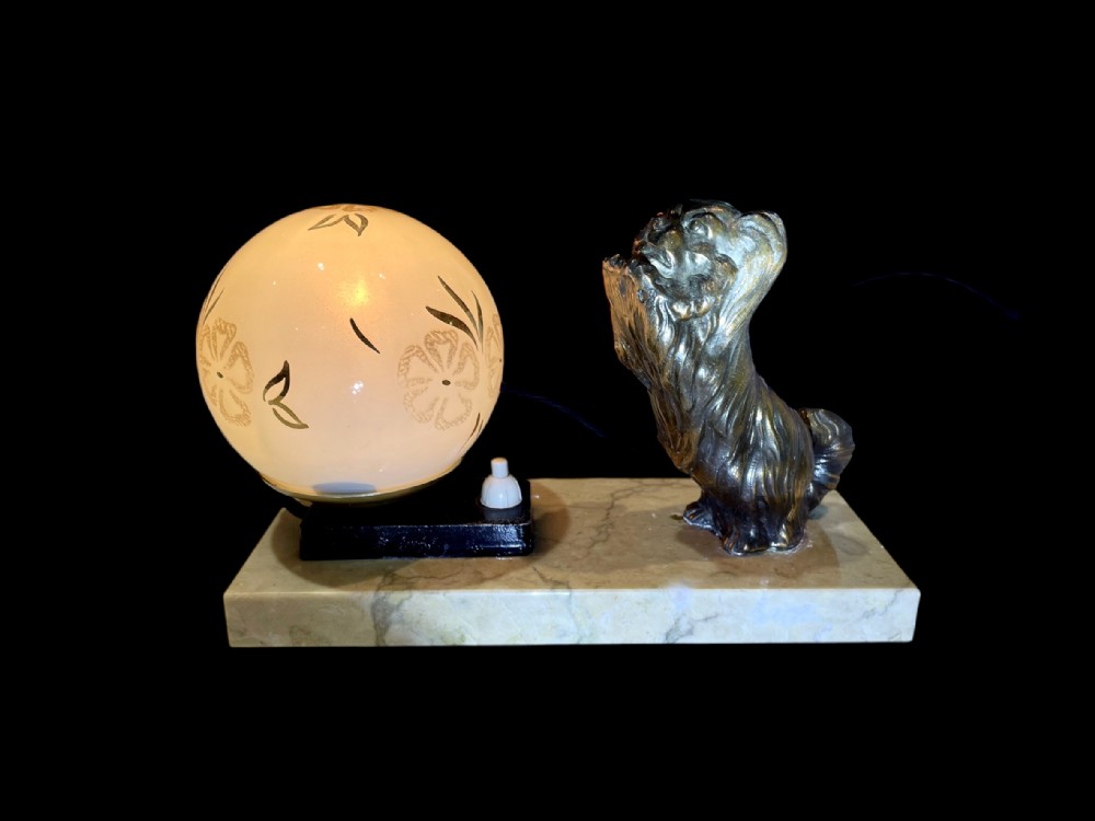 An Art Deco mood lamp featuring a metallic dog figure sitting beside an etched frosted glass globe shade on a rectangular beige marble base.