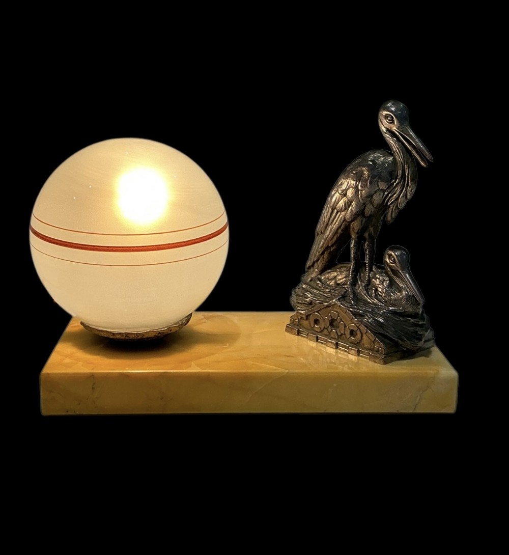 An Art Deco table lamp featuring a frosted spherical glass shade with orange striping alongside a silvered bird sculpture on a rectangular marble plinth.