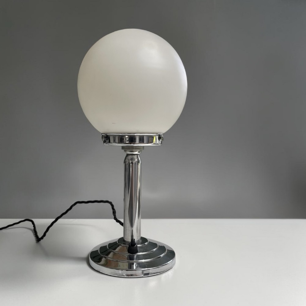 An Art Deco table lamp featuring a spherical white opal glass shade mounted on a polished chrome stem and stepped circular base.