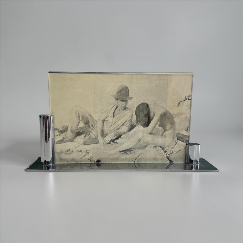 An Art Deco horizontal picture frame featuring a flat chrome base with cylindrical side supports holding a clear glass pane.