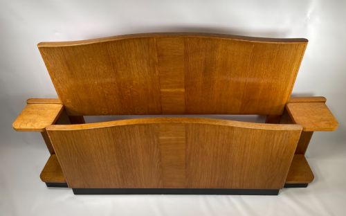 fig 1. An Art Deco oak bed featuring a gently curved headboard and matching footboard with integrated bedside tables on a dark ebonised plinth base.
