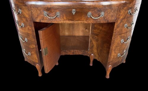 fig 2. A curved Art Deco burr walnut pedestal desk featuring a figure-matched grain top, central drawer, and multiple side drawers with metal handles.