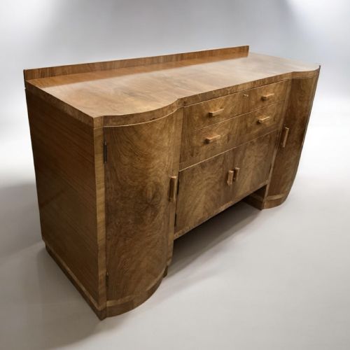 fig 1. An Art Deco burr walnut sideboard featuring curved side cupboard doors, central drawers, integrated timber handles, and a low rear upstand.