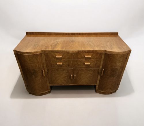 fig 2. An Art Deco burr walnut sideboard featuring curved side cupboard doors, central drawers, integrated timber handles, and a low rear upstand.