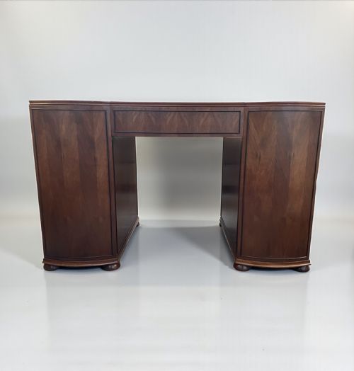 fig 1. An Art Deco walnut pedestal desk featuring curved front pedestals, multiple drawers with circular handles, and a central kneehole section.