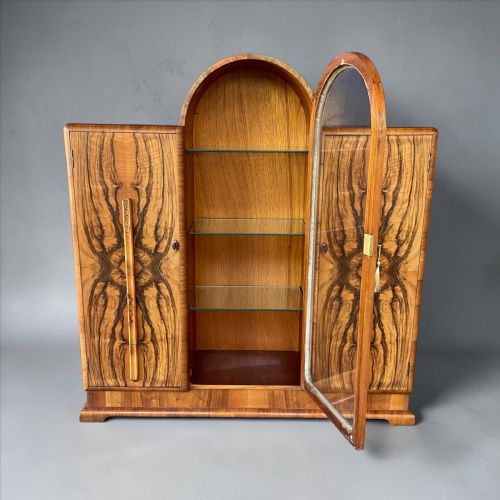 fig 1. An Art Deco walnut display cabinet featuring a central arched glazed door flanked by two side doors with symmetrical book-matched wood grain pattern.
