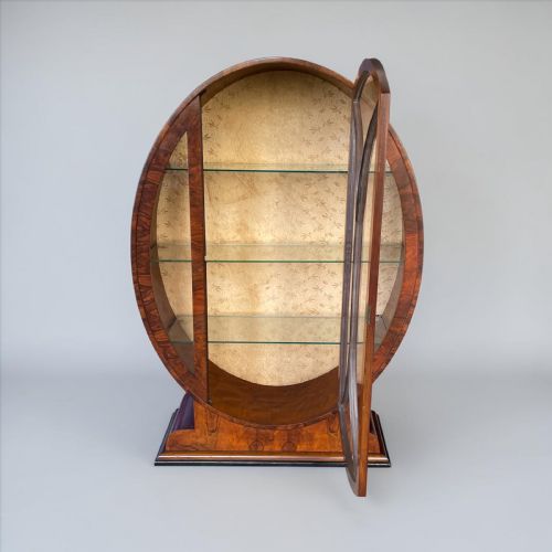 fig 1. An oval Art Deco display cabinet in figured walnut veneer with central glazed doors, glass shelves, and a patterned fabric interior.