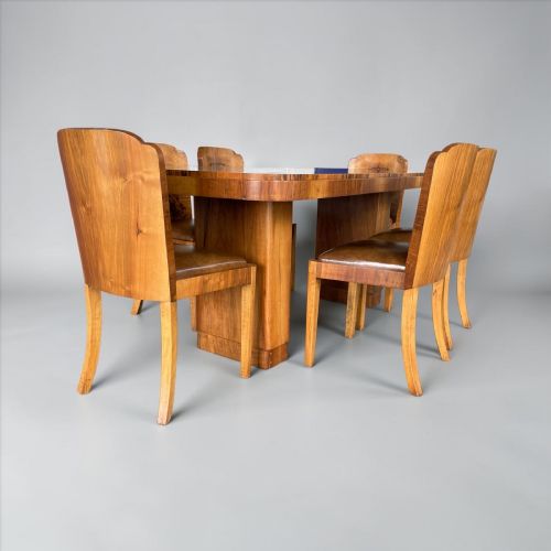 fig 1. An Art Deco burr walnut dining table accompanied by six matching chairs with curved backrests and dark brown leather seats.