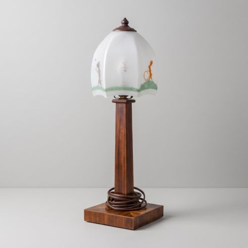 fig 1. An Art Deco table lamp featuring a square parquetry wooden base, a tall central column stem, and a frosted glass shade decorated with painted illustrations of animals.