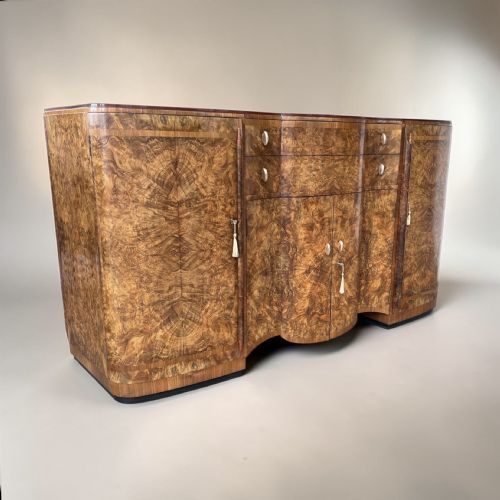 fig 1. An Art Deco burr walnut sideboard featuring a contoured front, book-matched timber veneers, central double doors, flanking side cupboards, and metallic handles.