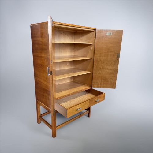 fig 1. An Art Deco golden oak cabinet on stand featuring book-matched chevron wood veneers, two lower drawers, twin cupboard doors, and metal handles.