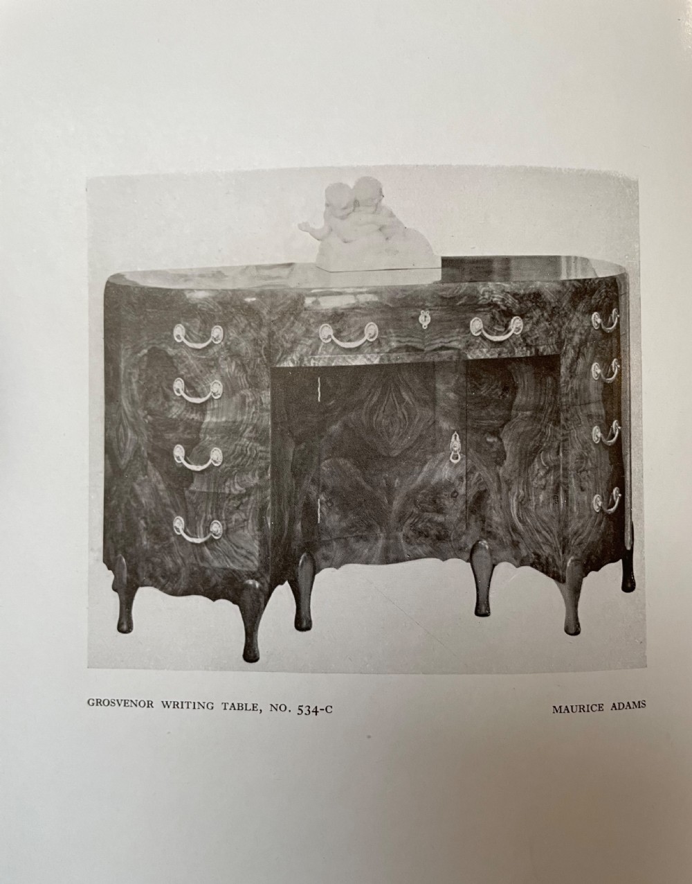 A curved Art Deco burr walnut pedestal desk featuring a figure-matched grain top, central drawer, and multiple side drawers with metal handles. View XV