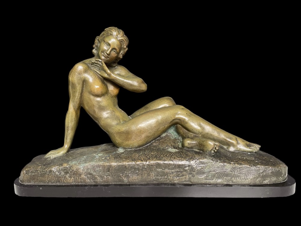An Art Deco bronze sculpture depicting a reclining female nude figure set on a moulded naturalistic base.