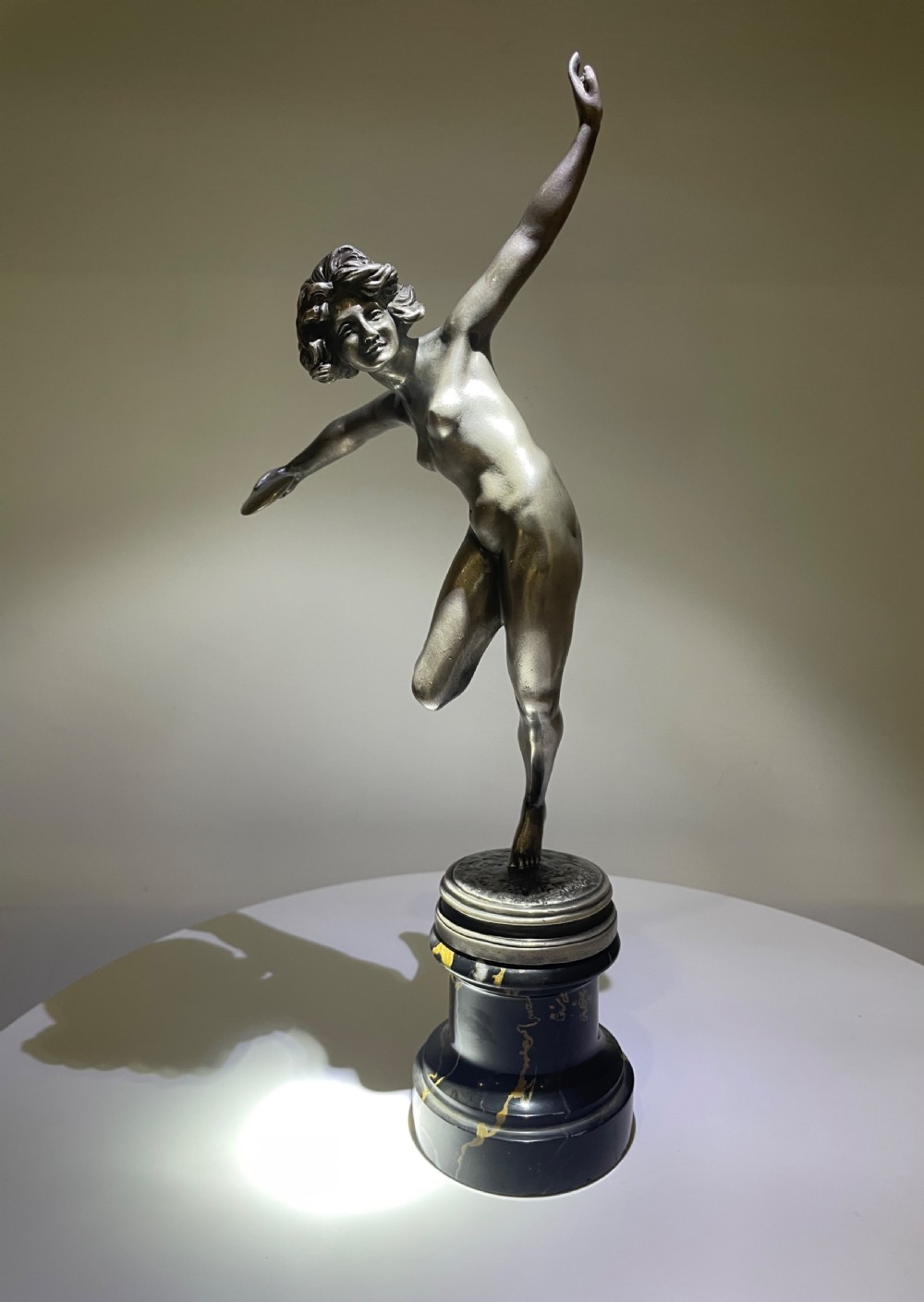 An Art Deco silvered bronze sculpture depicting a dynamic female figure posed on one leg atop a black veined marble pedestal. View VII