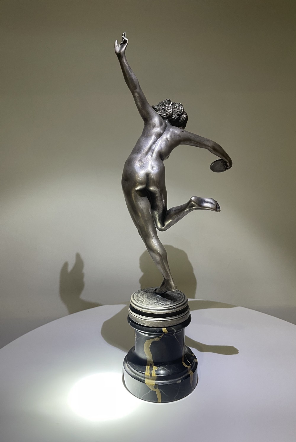 An Art Deco silvered bronze sculpture depicting a dynamic female figure posed on one leg atop a black veined marble pedestal. View IV