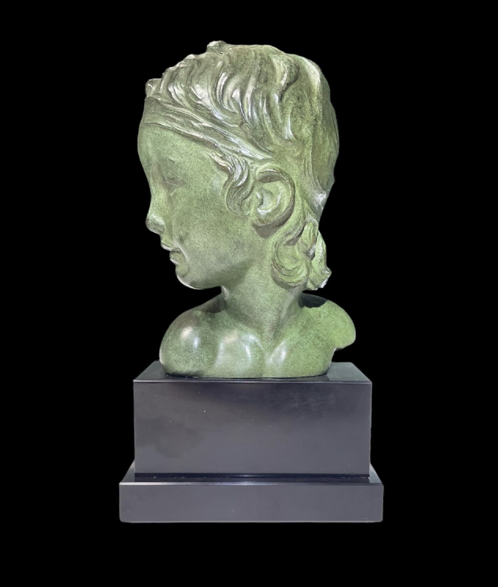 An Art Deco patinated green bronze profile bust of a child, mounted on a polished black rectangular marble base.