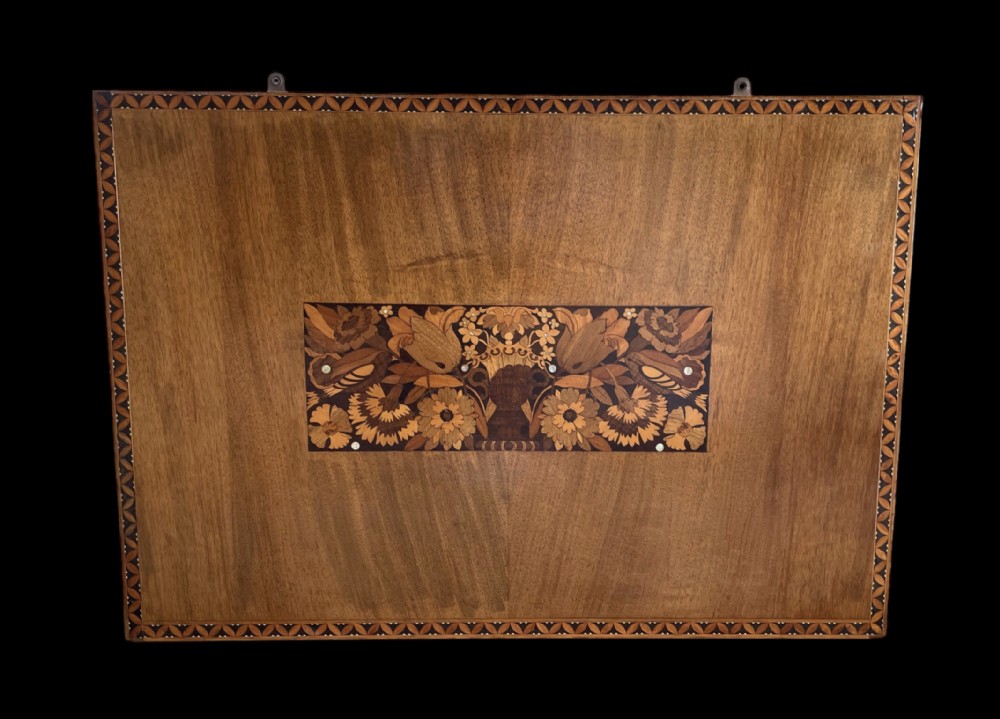 A rectangular warm brown wooden panel with an inlaid floral marquetry design in the centre and a geometric decorative border.