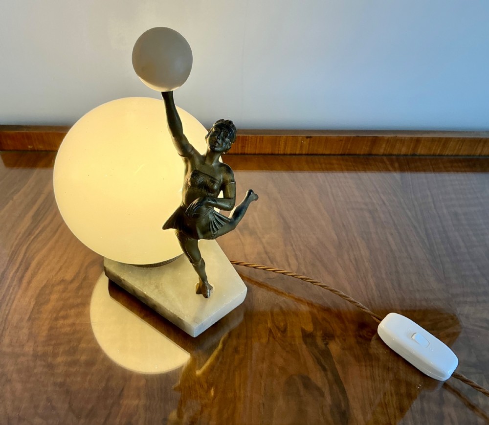 An Art Deco table lamp featuring a bronze figurine of a dancing lady posed beside a spherical frosted glass shade set on a marble base. View V