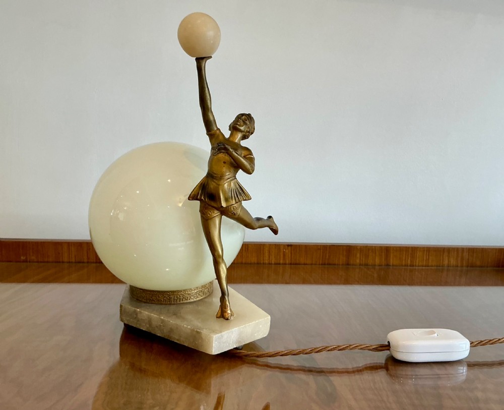 An Art Deco table lamp featuring a bronze figurine of a dancing lady posed beside a spherical frosted glass shade set on a marble base. View VI