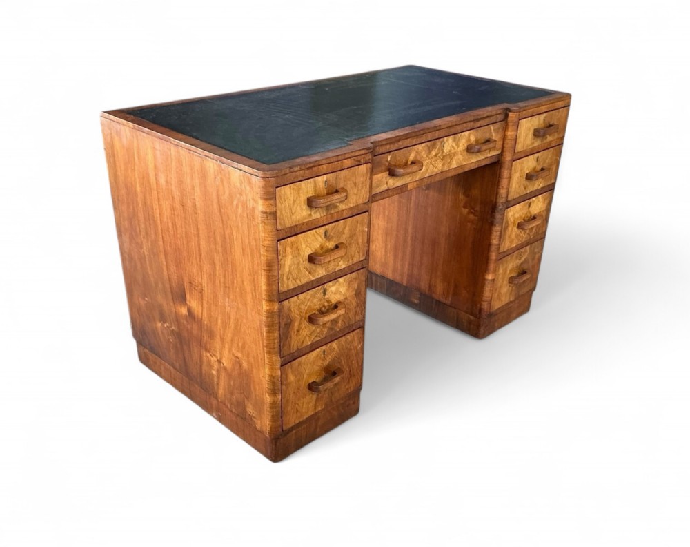 An Art Deco burr walnut pedestal desk with a dark green leather inset writing top and nine drawers with wooden handles.