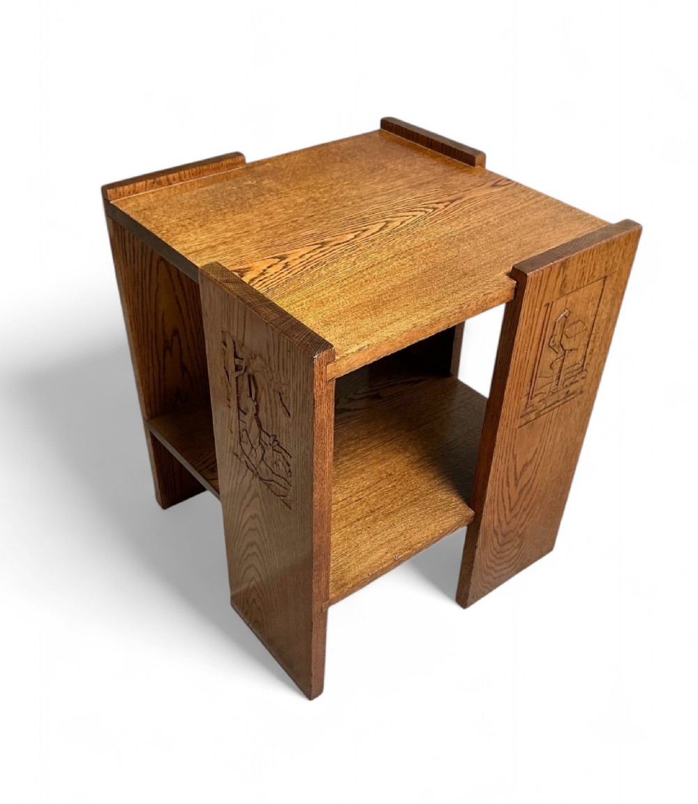 A square wooden Art Deco side table featuring carved geometric panels on the legs and a lower tier shelf.