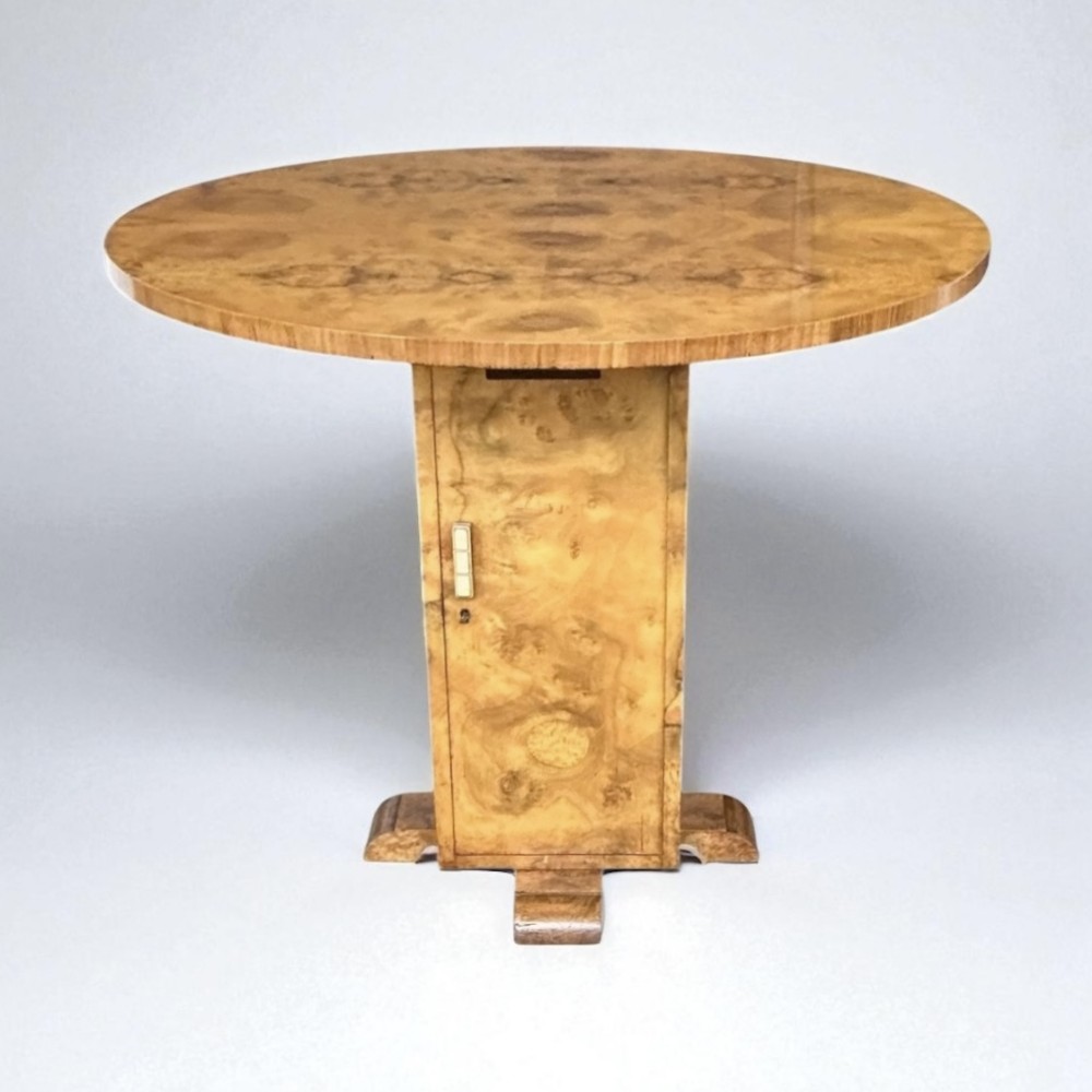 An antique round Art Deco centre dining table featuring prominent burr walnut veneer, a central pedestal base, and a compact cabinet compartment.