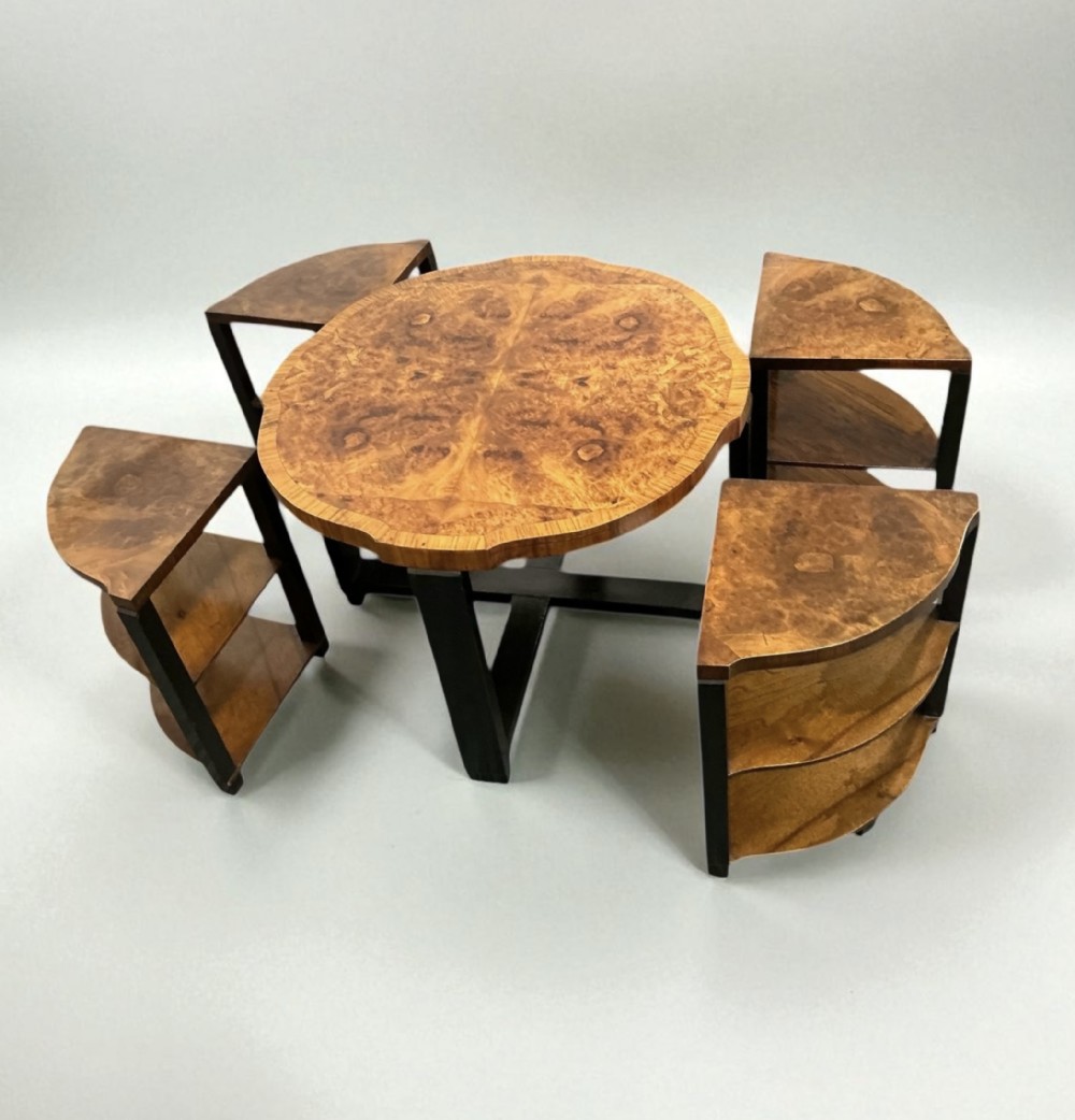 An Art Deco nest of tables featuring a circular central burr walnut top supported on an ebonised base, surrounded by four pie-shaped nesting side tables with matching veneered tops.