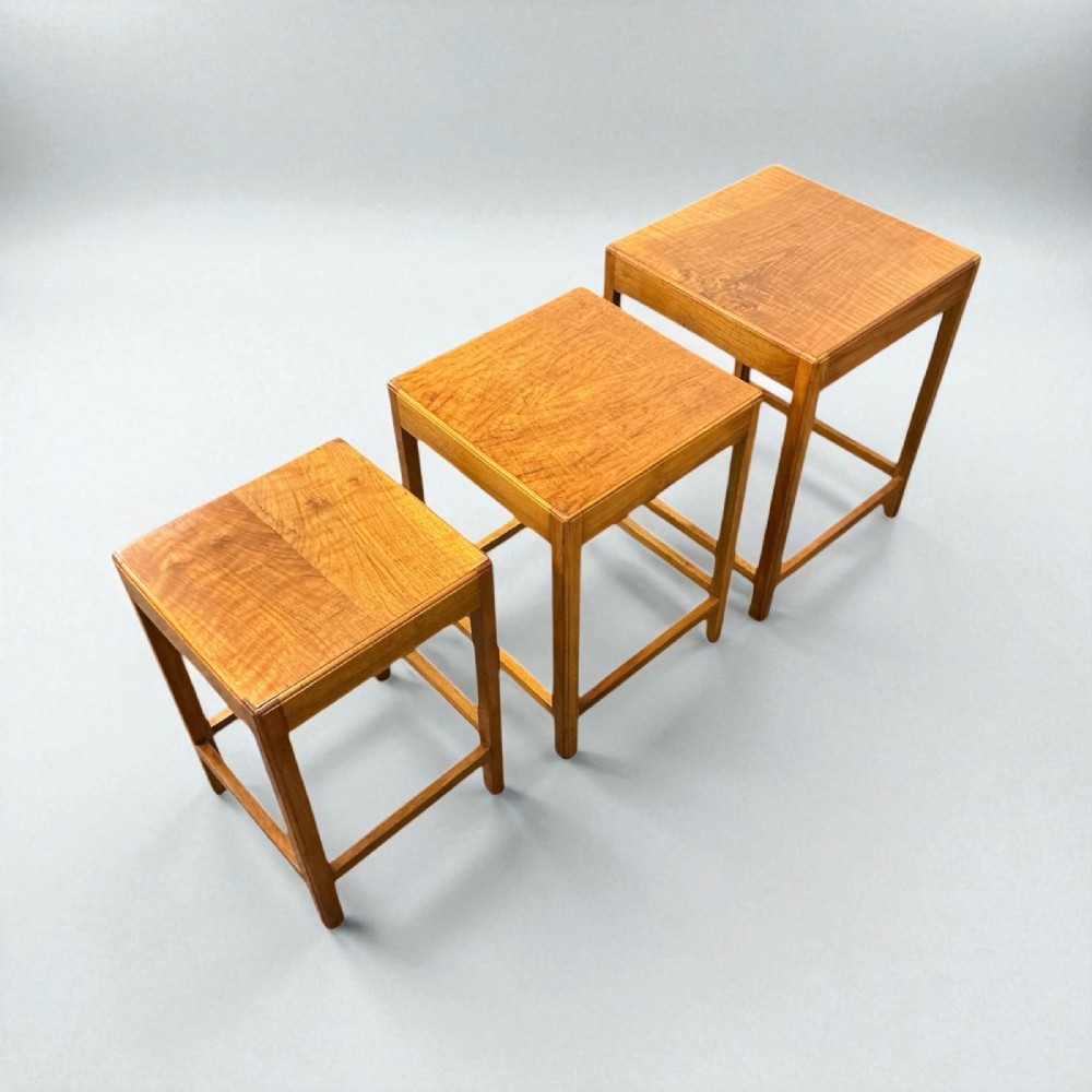 A set of three graduated square wood nest of tables with geometric frames and figured grain tops.