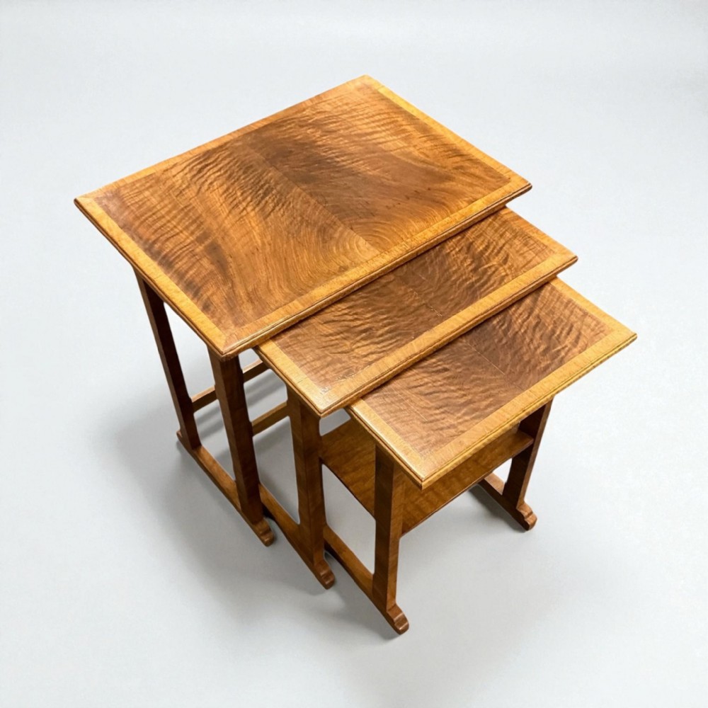 A set of three graduated Art Deco nesting side tables crafted from figured warm brown wood with crossbanded top borders.