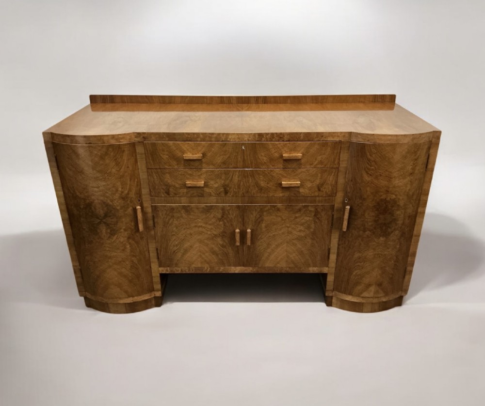 An Art Deco burr walnut sideboard featuring curved side cupboard doors, central drawers, integrated timber handles, and a low rear upstand.