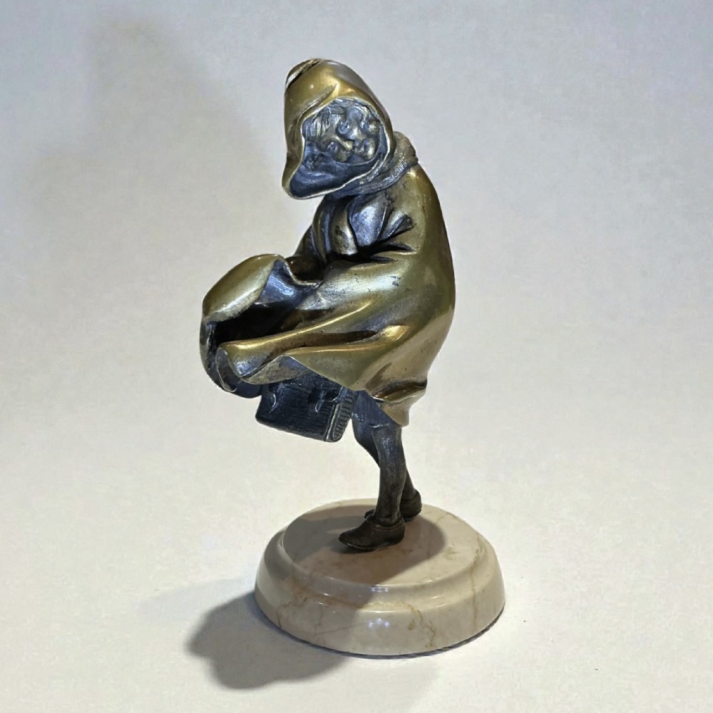 An Art Deco bronze sculpture of a hooded girl wearing a coat and carrying a bag, mounted on a round marble base.
