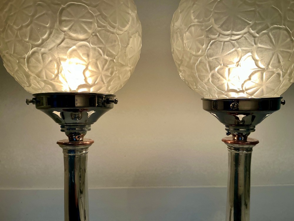 A pair of silver-toned Art Deco table lamps featuring fluted column stems and spherical frosted glass shades with moulded circular motifs. View IV