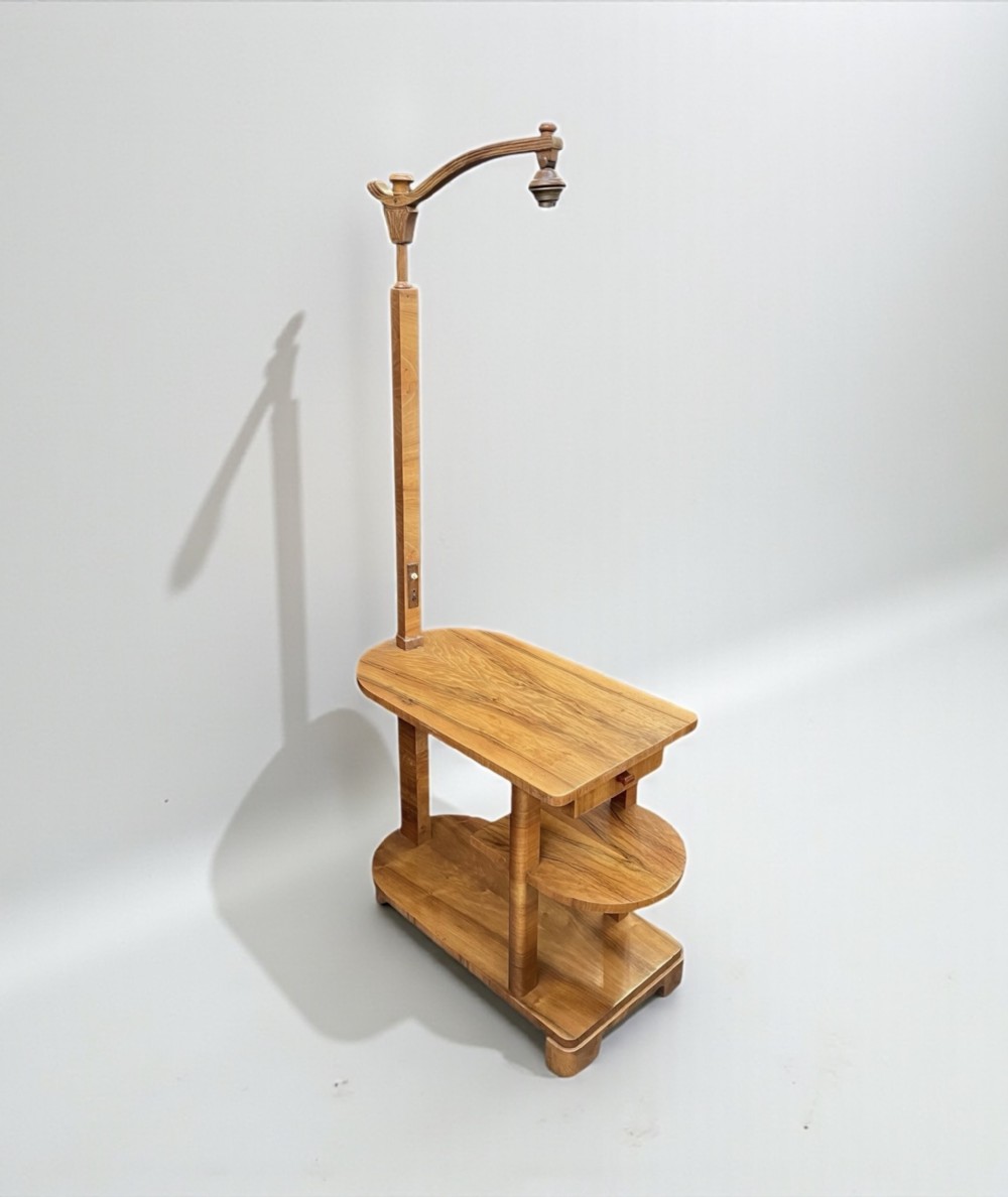 An Art Deco wooden lamp table featuring a rectangular surface, two lower tiered shelves, and an integrated vertical stem supporting an overhead curved light fixture.