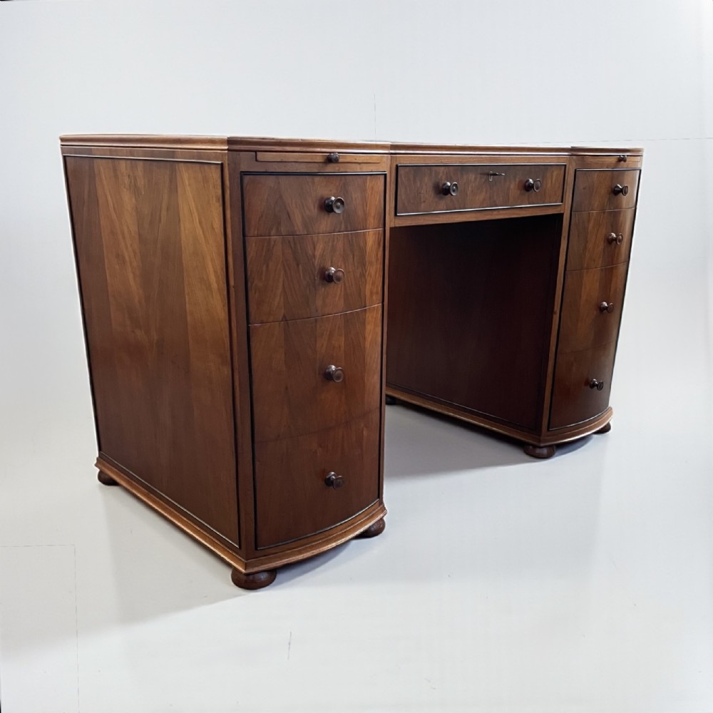 An Art Deco walnut pedestal desk featuring curved front pedestals, multiple drawers with circular handles, and a central kneehole section.