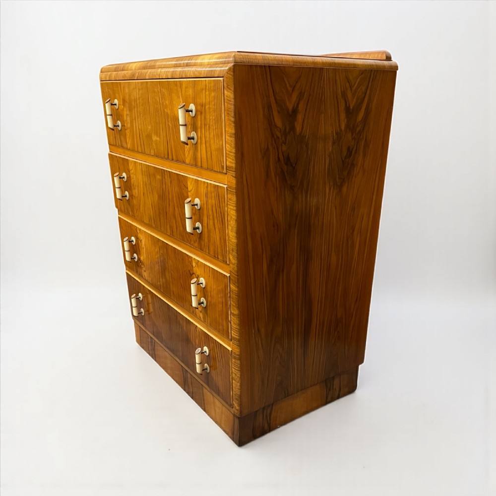 An Art Deco four-drawer chest constructed in warm brown walnut veneer with curved top edges and light-coloured vertical cylinder handles.