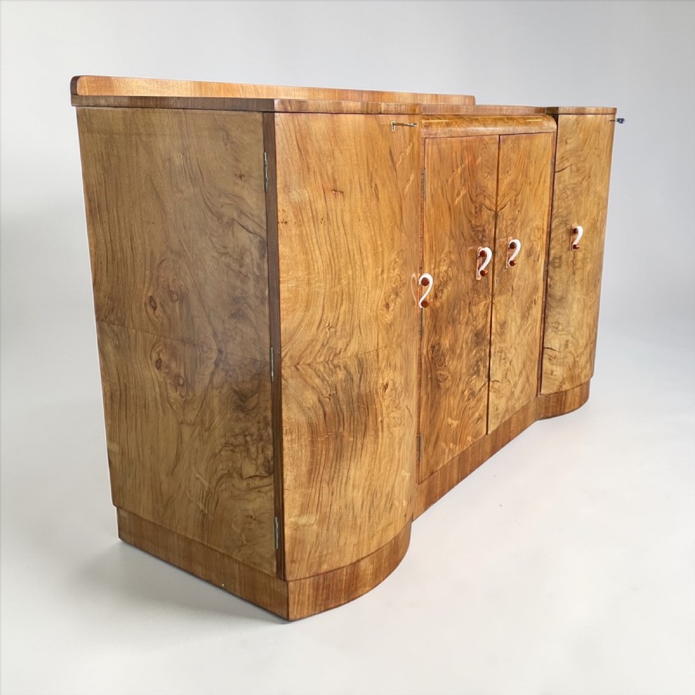 An Art Deco burr walnut sideboard featuring sweeping curved ends, four cabinet doors with stylized handles, and a continuous plinth base.