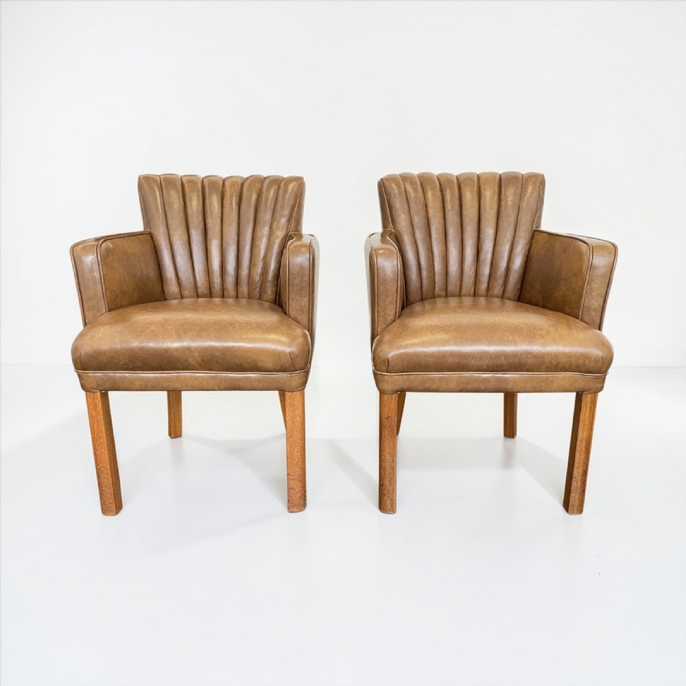 A pair of Art Deco armchairs upholstered in tan leather featuring vertical fluted backrests and square timber legs.