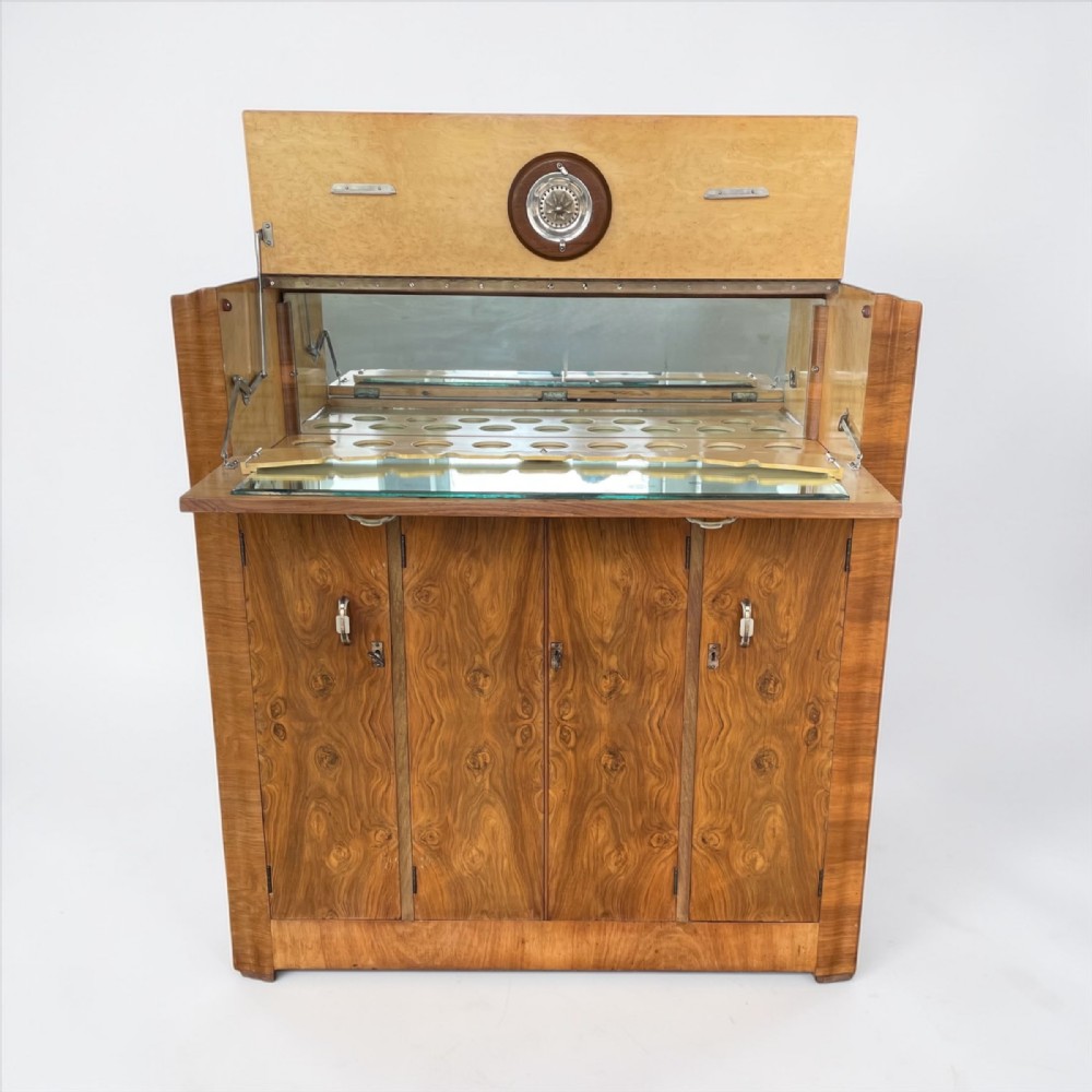 An Art Deco burr walnut cocktail cabinet shown open, displaying a mirrored fitted interior with glass shelving and lower cupboard doors.