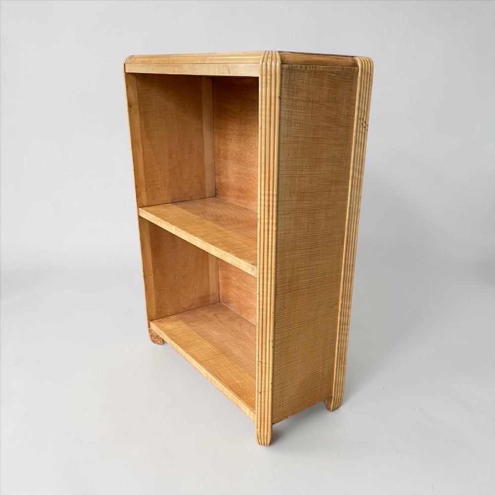 A small Art Deco light wood open bookcase with two shelves and vertical reeded moulding along the outer edges.
