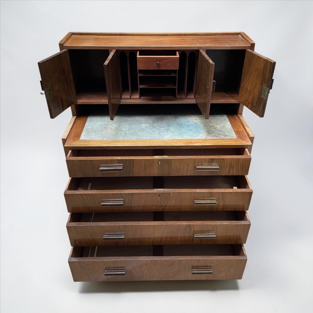 A compact walnut bureau featuring a fitted upper cabinet with small doors, a pull-out writing surface, and four wide lower drawers with wooden bar handles.