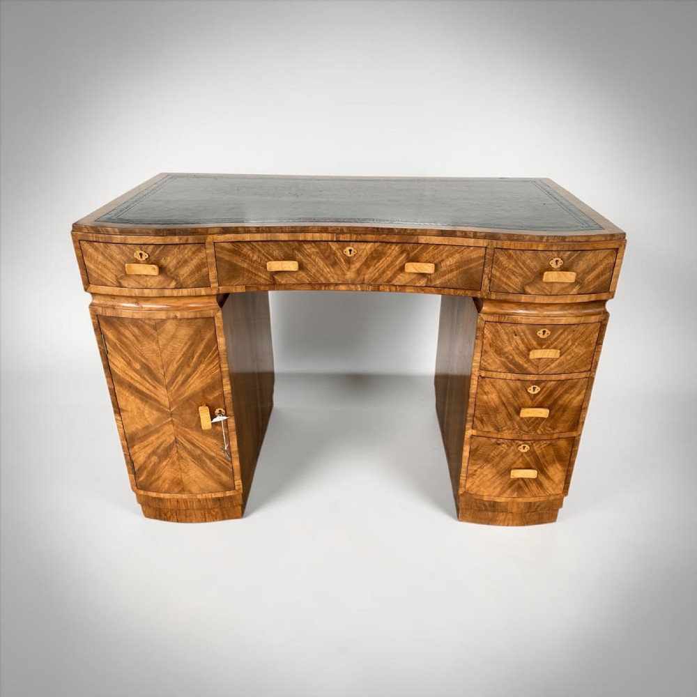 An Art Deco walnut pedestal desk featuring a green leather inset writing surface, sunburst veneer drawer fronts, and wooden handles.