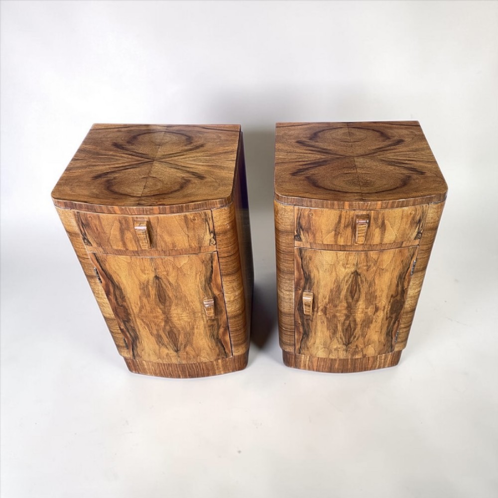 A matching pair of Art Deco walnut bedside cabinets featuring book-matched wood grain, single top drawers, rounded sides, and lower cupboard doors. View V