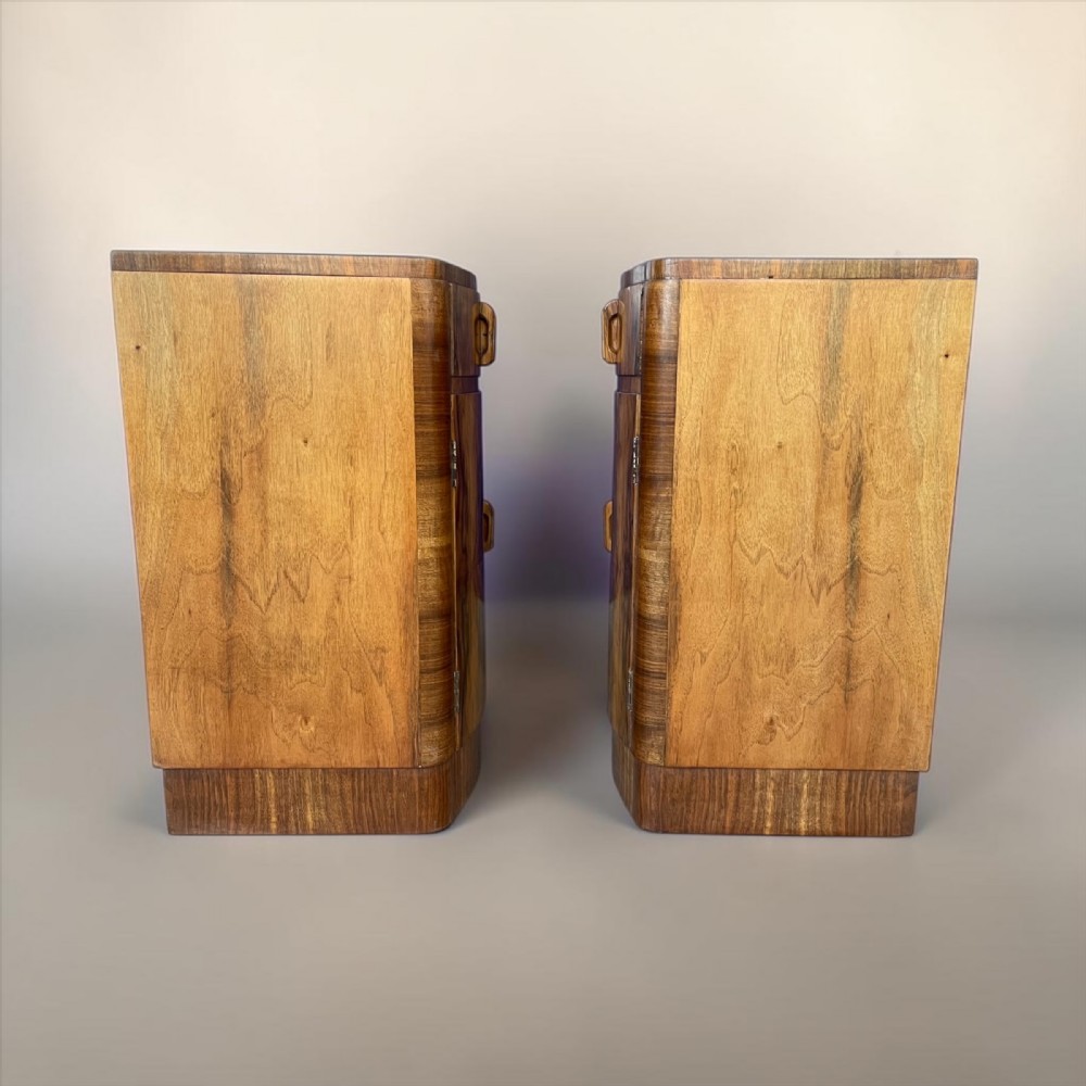 A matching pair of Art Deco walnut bedside cabinets featuring book-matched wood grain, single top drawers, rounded sides, and lower cupboard doors. View VI