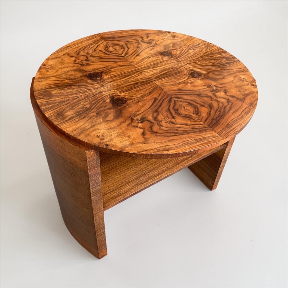 A circular Art Deco coffee table made of figured walnut veneer with a quartered top pattern, curved side supports, and an lower shelf.