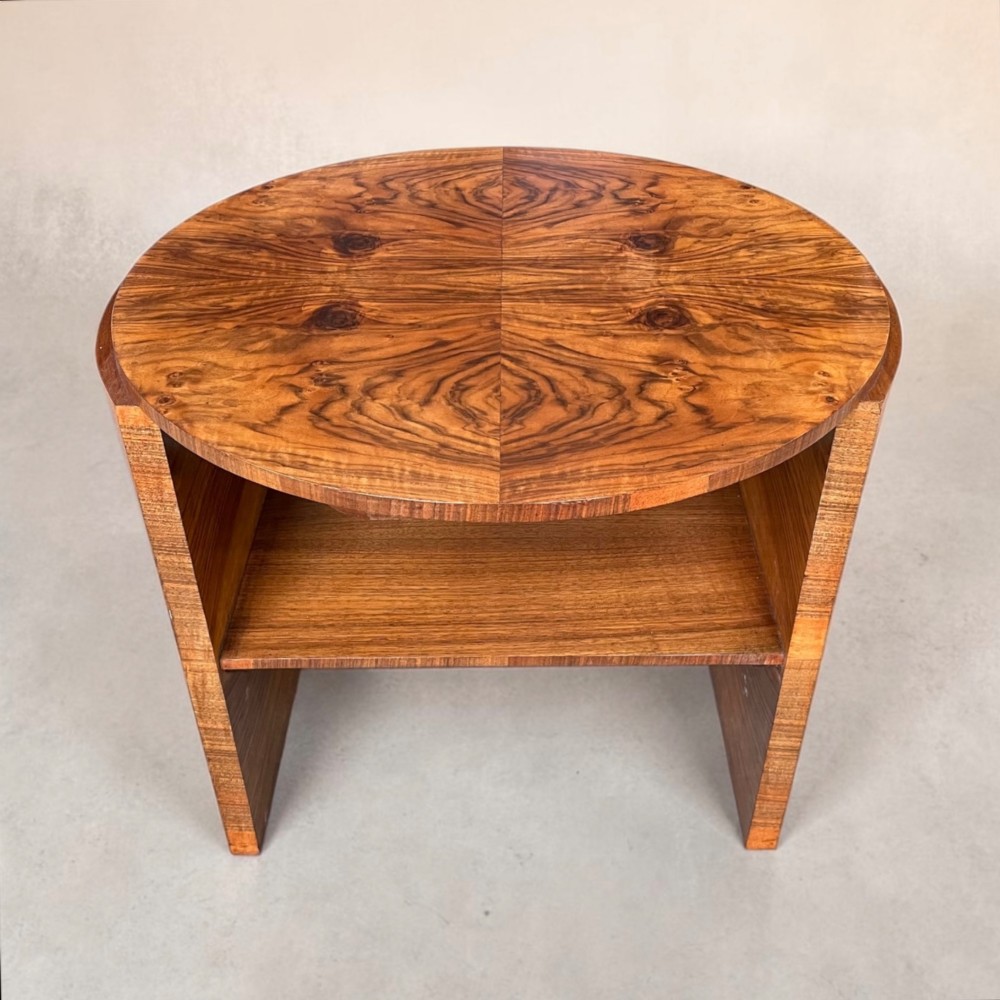 A circular Art Deco coffee table made of figured walnut veneer with a quartered top pattern, curved side supports, and an lower shelf. View II